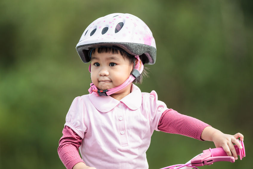 Photo of a girl wearing a helmet, riding a pink bicycle