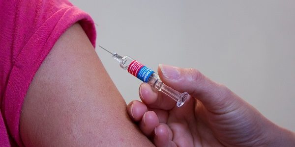 A photo of someone hold a needle to someone's upper arm area (vaccinate)